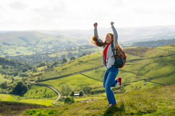 A joyful hiker leaps in celebration atop a green hill during a sunny day in the countryside