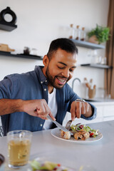 Smiling african american man eating chicken legs and fresh salad near herbal tea at home