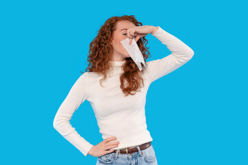 Woman with curly hair pinches her nose while holding a letter against a bright blue background,...