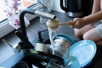 Young boy's hand washing dishes with a brush in a black sink
