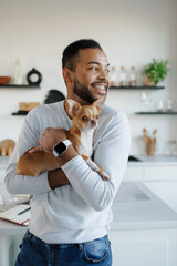 Smiling african american man holding chihuahua dog in kitchen at home