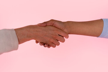 Two hands engage in a handshake against a soft pink background, symbolizing agreement and...
