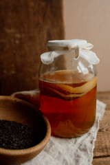 Glass jar with kombucha drink and wooden bowl with tea. Kombucha tea and ingredients