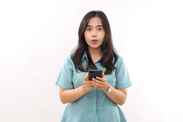 Shocked young Asian woman reacts on something very surprising stares with eyes popped out holds mobile phone, isolated over white wall