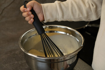 A small hand holds a black whisk and makes pancake batter in a silver bowl