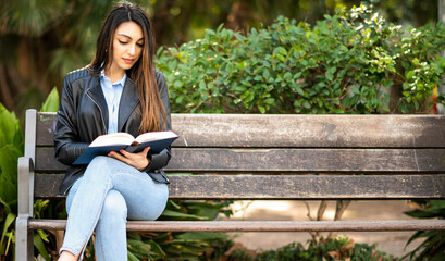 Beautiful female college student reading a book on a bench in a park