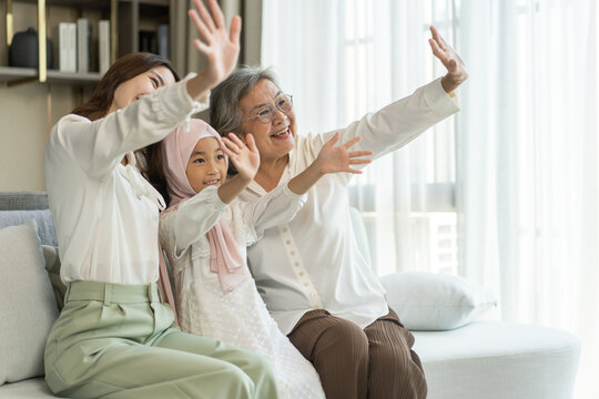 Multi generational asian family bonding at home, grandmother, mother, and daughter waving together, happy family moments, diverse family values, joyful connection, smiling and warmth, candid lifestyle