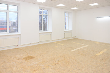 Bright spacious empty room with large windows, white walls, and ceiling lights in a modern building interior.