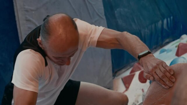 Top view shot of sporty middle-aged Caucasian man hanging on top of artificial climbing wall and jumping down to gym mat