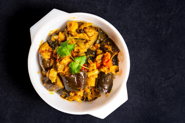 Homemade spicy aubergine curry with onions and tomatoes, in a serving bowl. Top view.