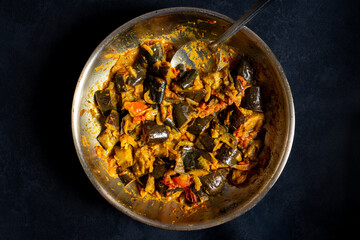 Homemade spicy aubergine curry with onions and tomatoes in a metal pan. Indian vegetarian dish. Top view.