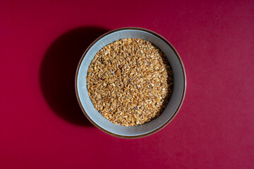 Golden linseed in a bowl on a red worktop. Top view.