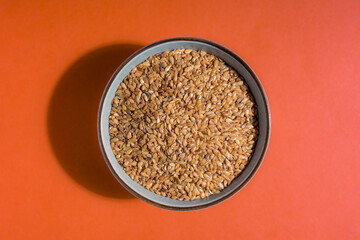 Golden linseed in a bowl on an orange worktop. Top view.