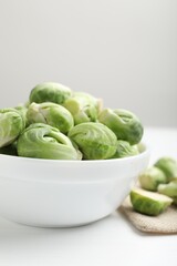 Fresh Brussels sprouts in bowl on white table, closeup