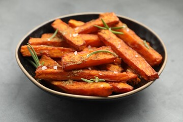 Delicious sweet potato fries with spices in bowl on grey table, closeup