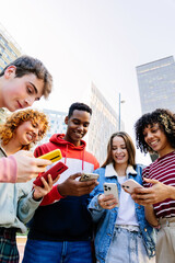 Vertical shot of young group of teenage student people having fun using mobile phone together outdoors. Multiracial friends watching social media content on cellphone app. Youth and technology concept