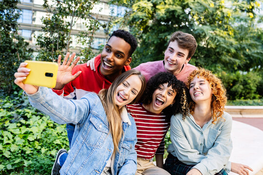 Young diverse group of young people having fun taking selfie portrait sitting together outdoors while enjoying free time at city street. Gen Z students posing for photo at campus college.