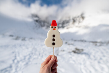 Snowman shaped lollipop held in a hand. In the background beautiful snowy landscape with...
