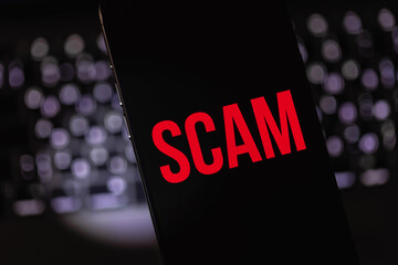 closeup mobile smartphone with red text SCAM on a black screen