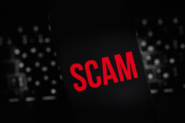 mobile smartphone with red text SCAM on a black screen closeup