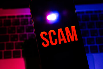 smartphone with red text SCAM on a black screen with police lights flashing