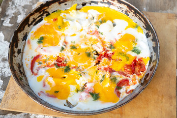 scrambled eggs cooked in a frying pan with tomatoes and herbs, outside