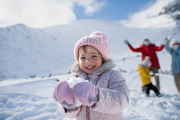 Portrait of small girl enjoying winter holiday in the mountains with family, playing in snow,...