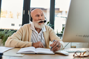 Naklejka premium A savvy senior professional with a beard conducts a virtual meeting in a bright, stylish office space.