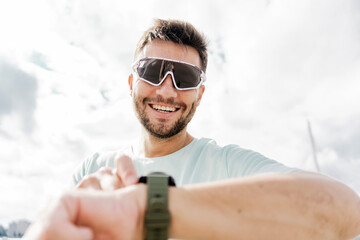 A Cheerful Man Wearing Sunglasses Checks the Time on His Watch While Enjoying a Sunny Day Outdoors