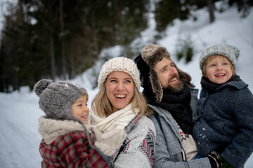 Young family is enjoying winter holiday in the mountains, standing in the middle of snowy forest.