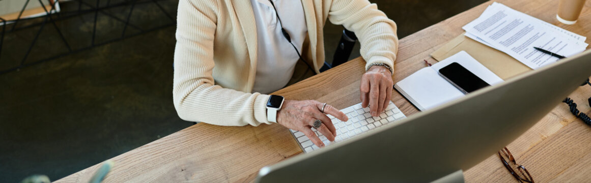 A stylish senior businessman focuses on his work, typing on a sleek keyboard in a contemporary office.