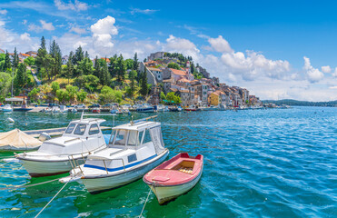 Serene harbor of Sibenik, Croatia, featuring boats docked along the Adriatic coast, historic buildings, and clear blue waters on a sunny day.
