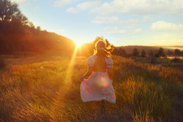 A girl in a  beautiful drees running in the sunset. Picture taken from the back.