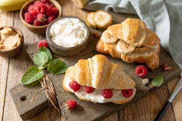 Breakfast concept, dessert french pastry. Tasty freshly baked open croissants with cream cheese and raspberry on a rustic background.