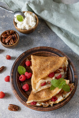 Tasty homemade sweet crepes stuffed with raspberries and cream cheese on a gray stone background. Thin pancakes, blini. Sweet dessert.