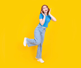 Happy excited woman, full body side view caucasian 20s happy excited woman wear casual jean and blue t shirt raise up leg puts hands on face screaming laughing out loud isolated on yellow background.