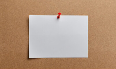 A blank white note is pinned to a brown corkboard with a red pushpin
