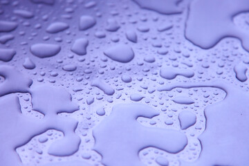 Close-up of water droplets on a smooth surface, forming unique shapes and patterns with a soft purple tint
