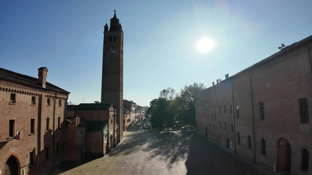 Sunlight shines on historic church Santa Maria in Castello and tower in Carpi, Italy, surrounded by ancient brick buildings on a clear day
