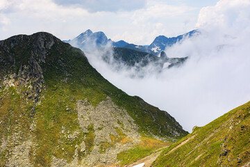 mountain landscape of romania in summer. rocky peak. fagaras ridge in clouds. alpine scenery on a sunny day. popular travel destination of europe. high altitude viewpoint. breathtaking extreme terrain