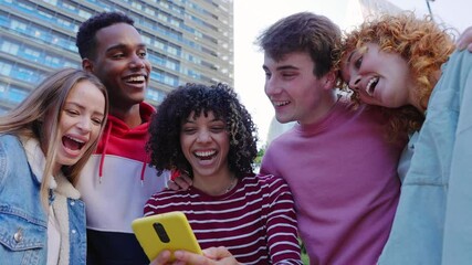 Happy young group of diverse teenage friends using mobile phone at city street. Generation Z people having fun watching media content on social platform app outside. Youth community concept