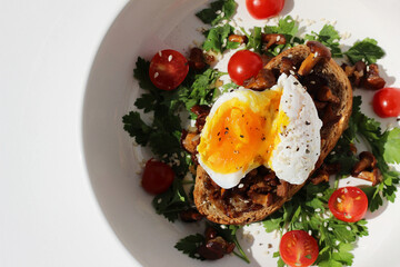 Breakfast. Poached Egg with Liquid Yolk on Toast with Fried Chanterelles, Garnished with Cut Cherry Tomatoes and Parsley.