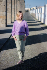 A woman stands near an ancient aqueduct on a sunny day, the bright sunlight casting dramatic shadows across the historic structure.