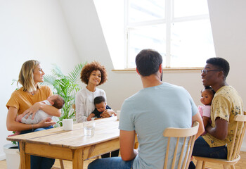 Two Families With Babies Meeting And Talking Around Table On Play Date At Home