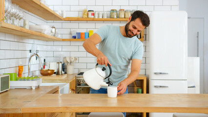 Young Man At Home Pouring Hot Water From Kettle Making Hot Drink In Modern Loft Apartment