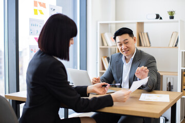 Caucasian businesswoman presents report to Asian businessman boss in modern office. Collaborative atmosphere as female employee discusses data with male manager emphasizing teamwork .