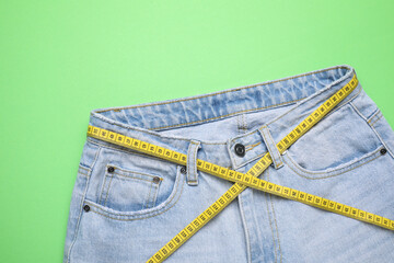 Jeans and measuring tape on green background, top view