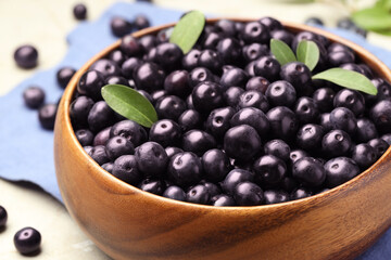 Ripe acai berries and leaves in bowl on grey table, closeup