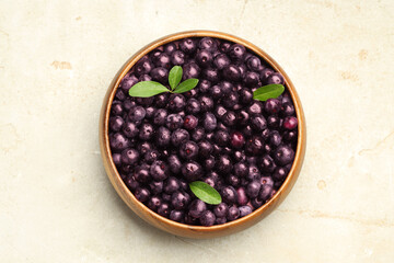 Ripe acai berries and leaves in bowl on light table, top view