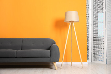 Stylish sofa and lamp near orange wall indoors